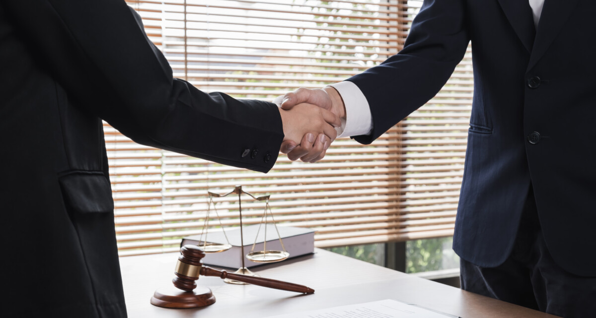A lawyer and a businesswoman shake hands and reach an agreement on a cooperation contract document. In the lawyer's office and there is a hammer lying on the table. A lawyer and a businesswoman shake hands and reach an agreement on a cooperation contract document. In the lawyer's office and there is a hammer lying on the table..
